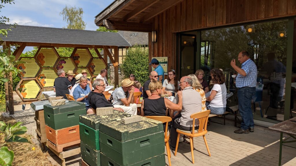 Mitglieder des Imkervereins Konz sitzen an einem sonnigen Tag am Lehrbienenhaus auf dem Roscheider Hof zusammen.